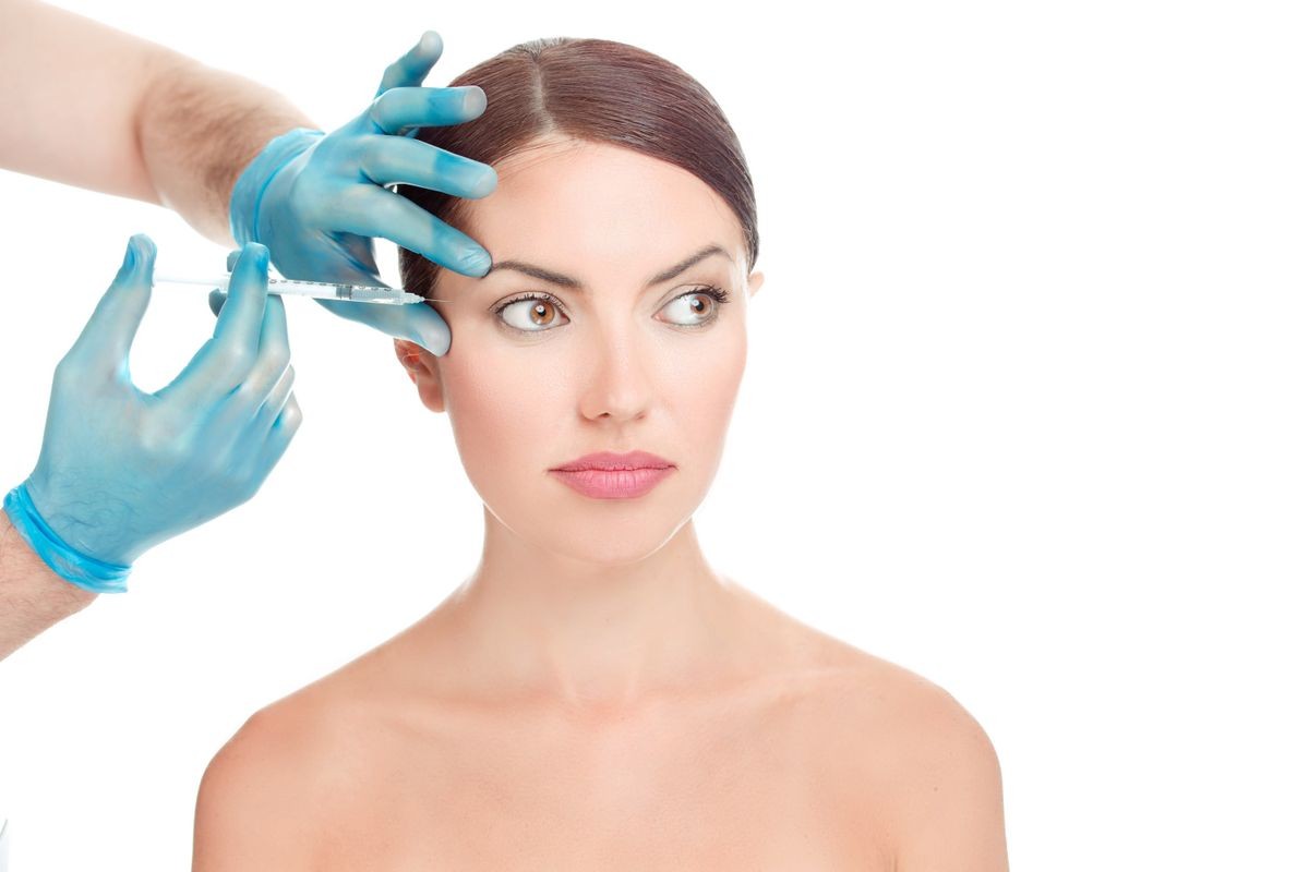 Woman having anti wrinkles, anti-aging serum shot around eyes plastic surgery done by doctor's hand in blue gloves holding injection over woman's face isolate on white background Face without wrinkles